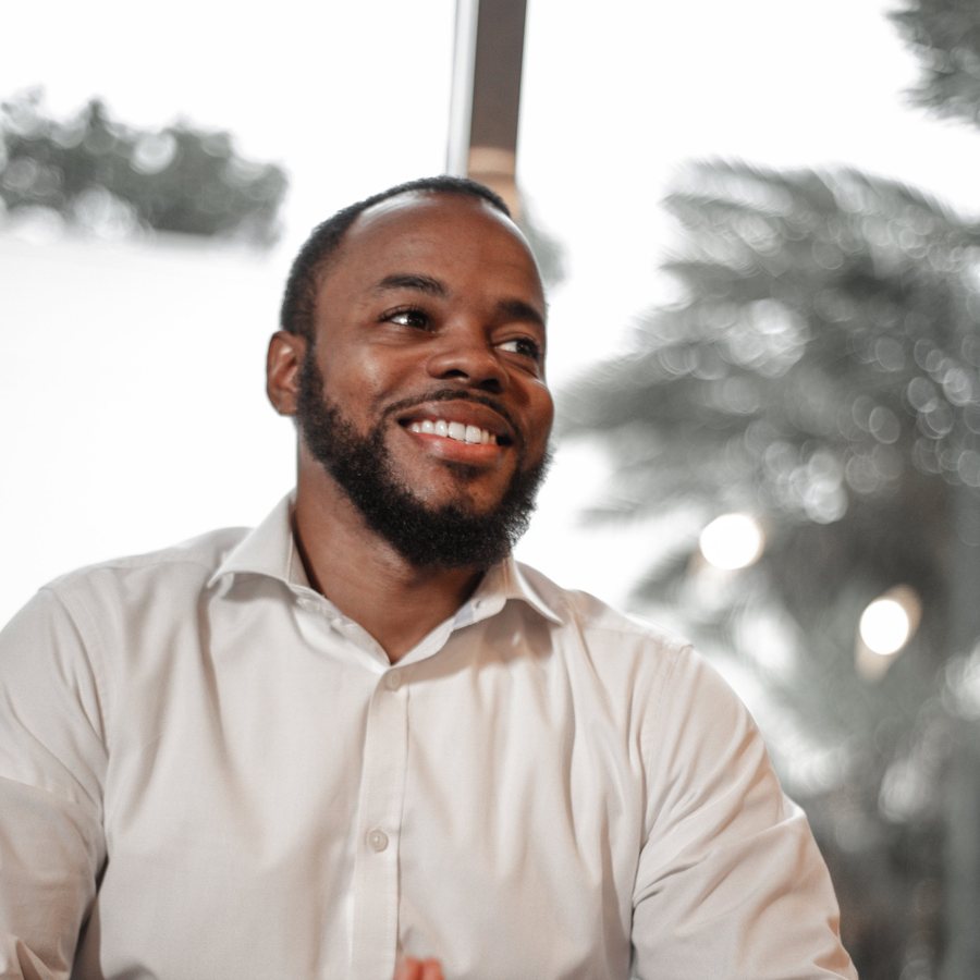 Kevin, Digital Presence Lead at TL Media Agency, seated in a white dress shirt with hands folded, looking aside and smiling
